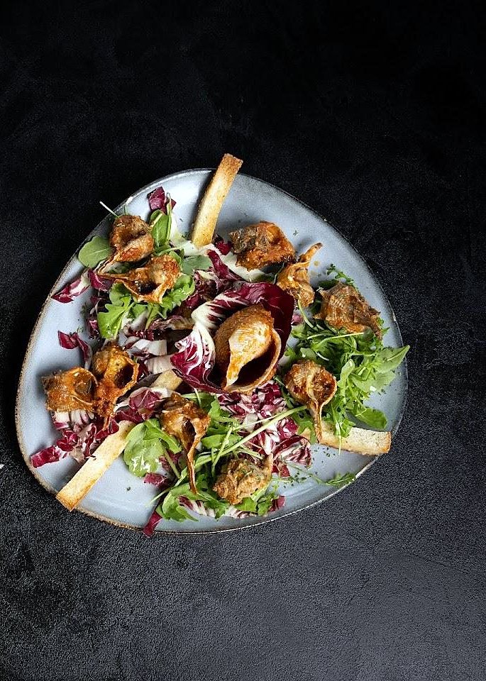 Antipasto su piatto azzurro con radicchio, rucola, lumachine e pane croccante
