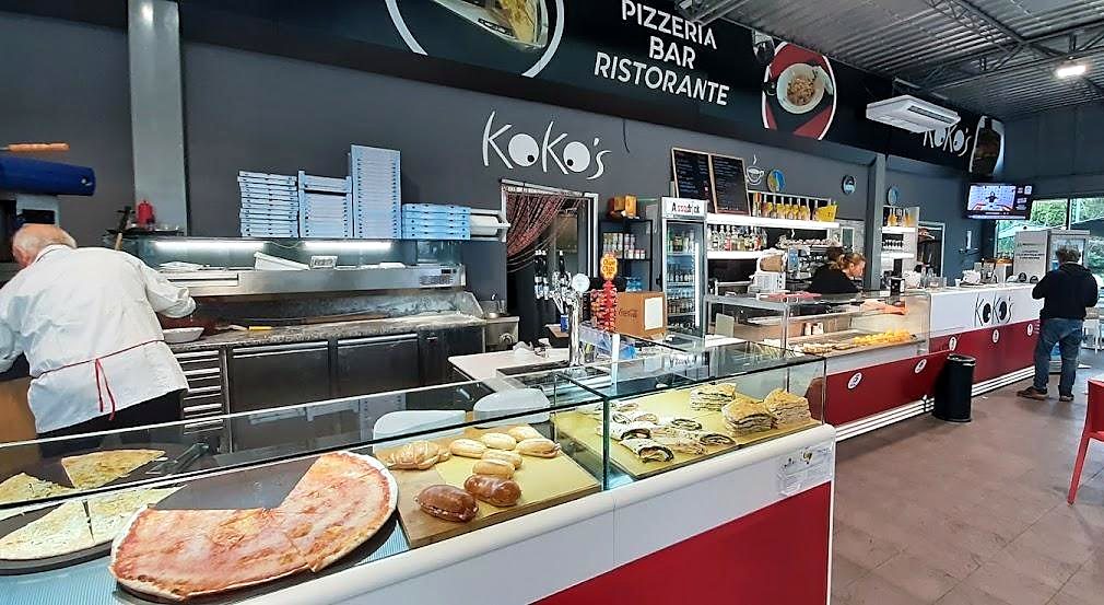 L'interno di Koko's: il banco rosso con le pizze, il forno e il pizzaiolo al lavoro